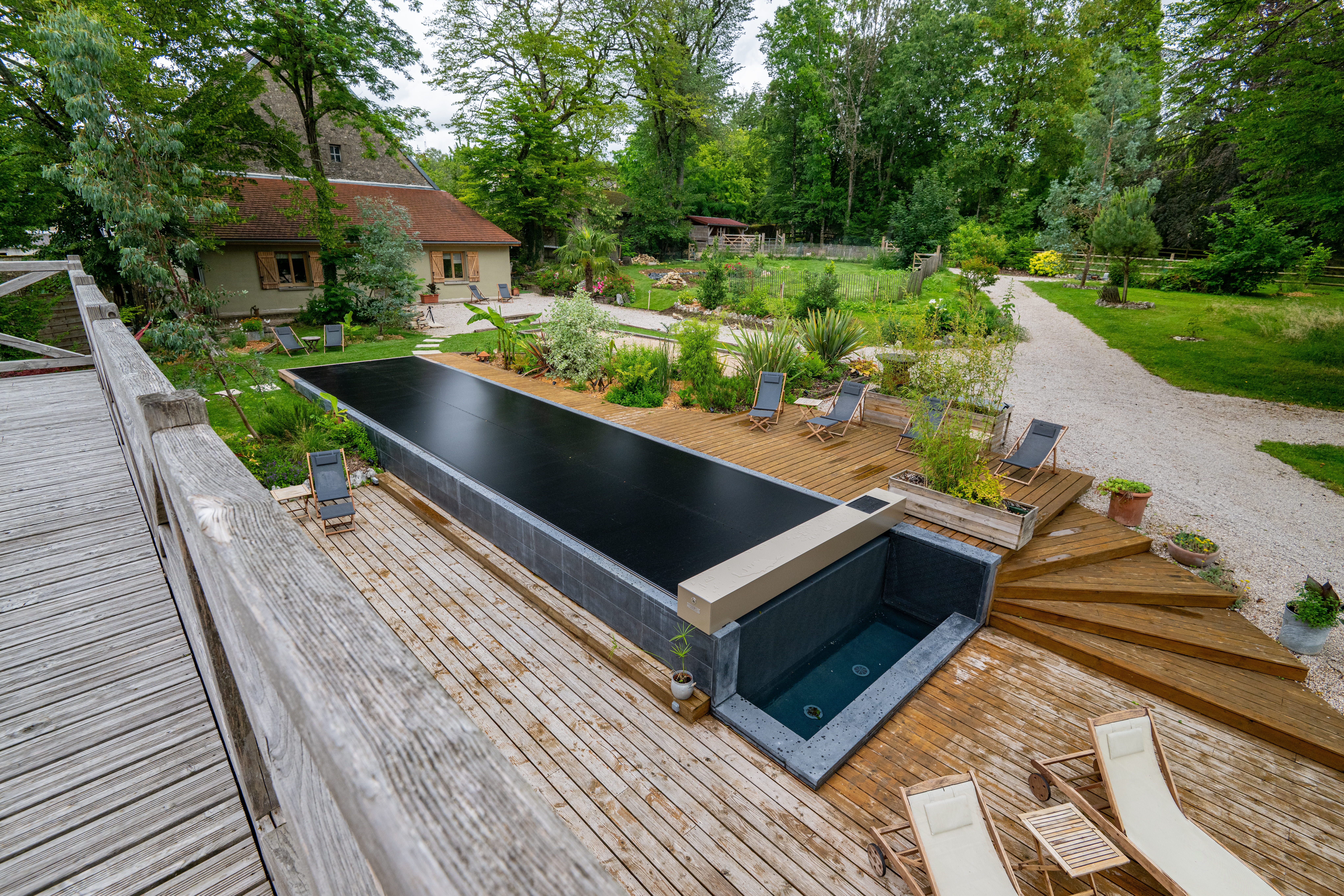 Vue en hauteur d’une piscine équipée d’une couverture Coverseal noire, entourée d’une terrasse en bois et d’un jardin paysager