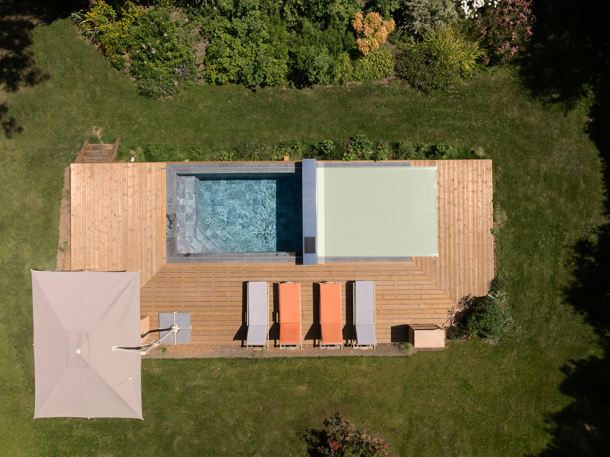 Vue aérienne d’une piscine partiellement recouverte par une couverture Coverseal vert clair, entourée d’une terrasse en bois et de transats.