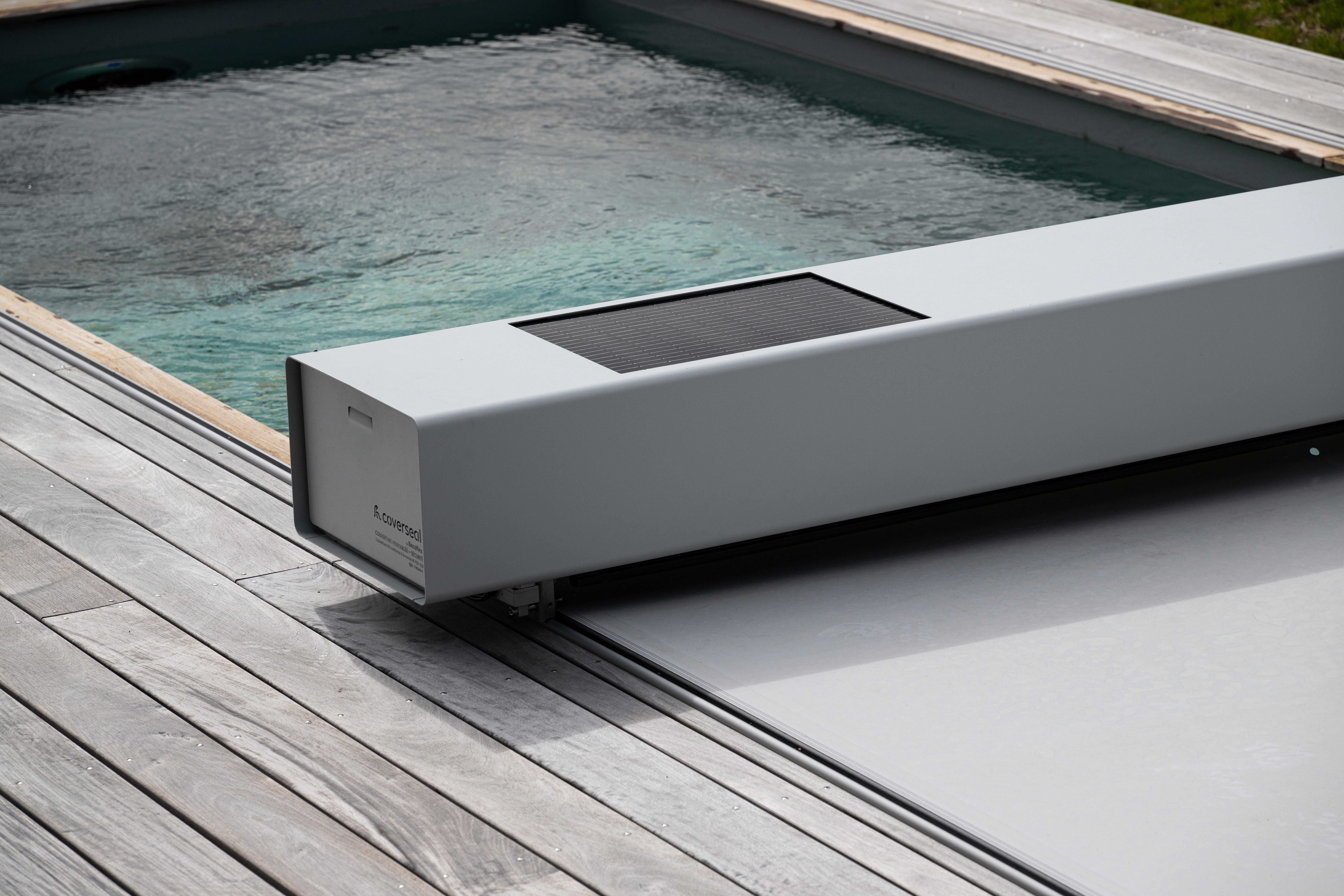 Couverture de piscine Coverseal gris clair installé en bord de piscine, avec membrane déployée.